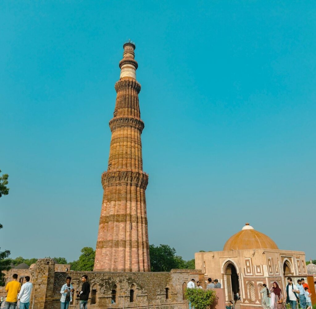 a tall tower with people around it with Qutub Minar in the background